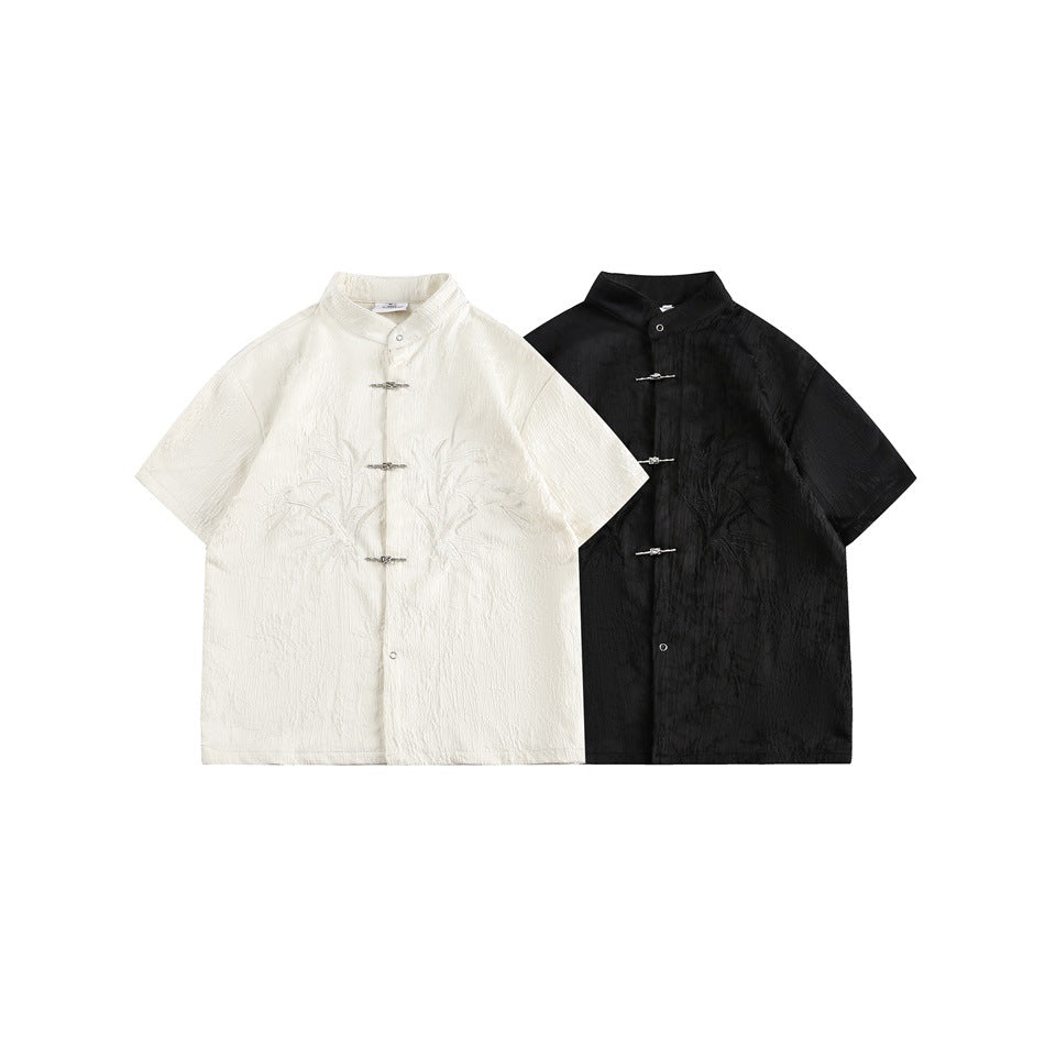 Ivory and black short-sleeve stand-collar shirts with botanical embroidery and silver frog closures, shown together.
