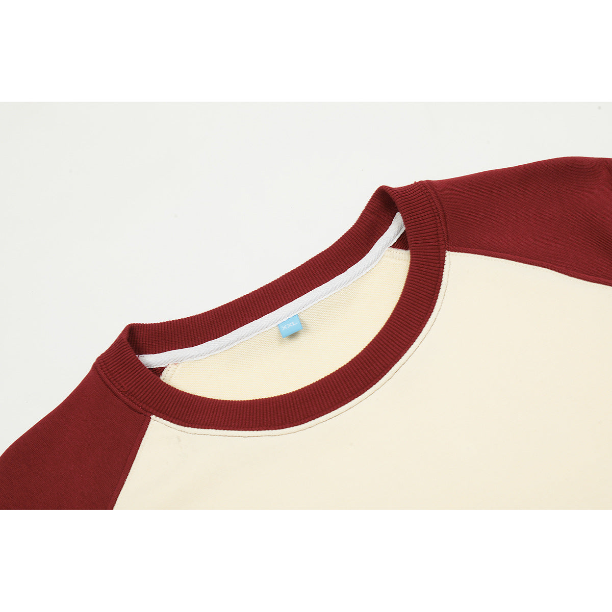 Close-up of a burgundy ribbed crew neckline and shoulder beside the cream body of a raglan sweatshirt.
