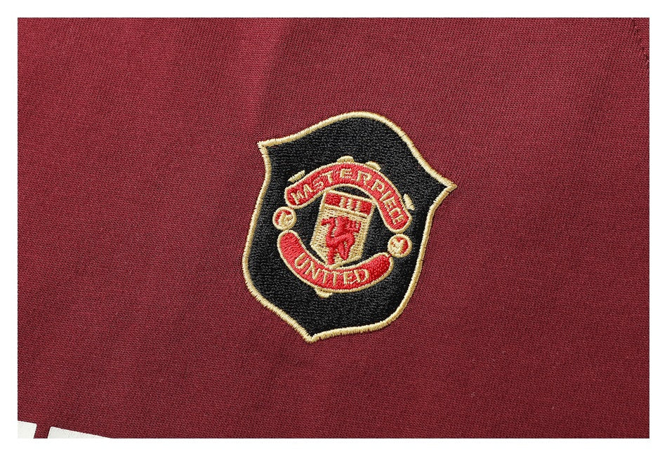 Close-up of an embroidered black, red and gold Manchester United crest on burgundy fabric.
