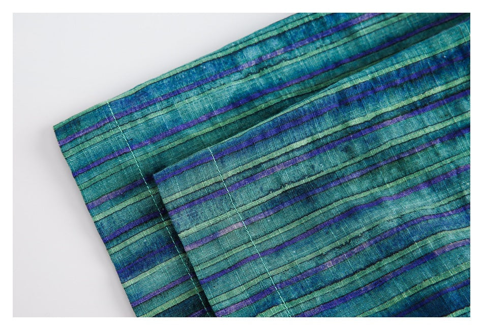 Close-up of teal fabric with narrow blue, green, and purple stripes and visible stitching.
