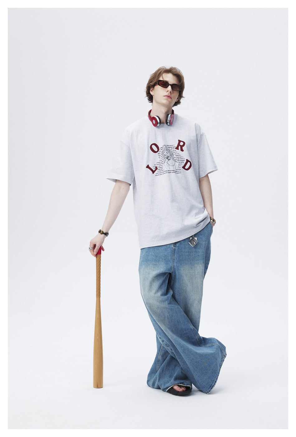 Model wears a light gray oversized graphic T-shirt with blue wide-leg jeans and sunglasses.