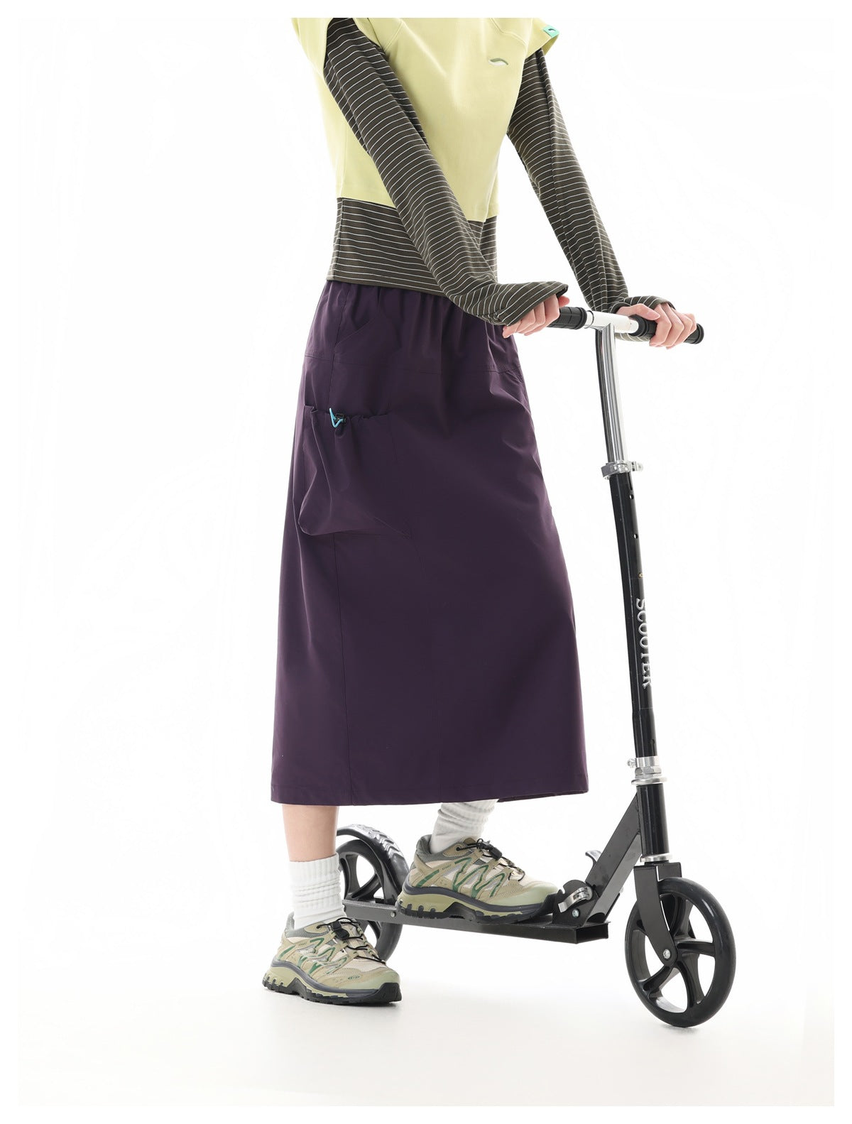 Side view of a model wearing a dark plum midi skirt with a large pocket and drawcord detail, beside a scooter.