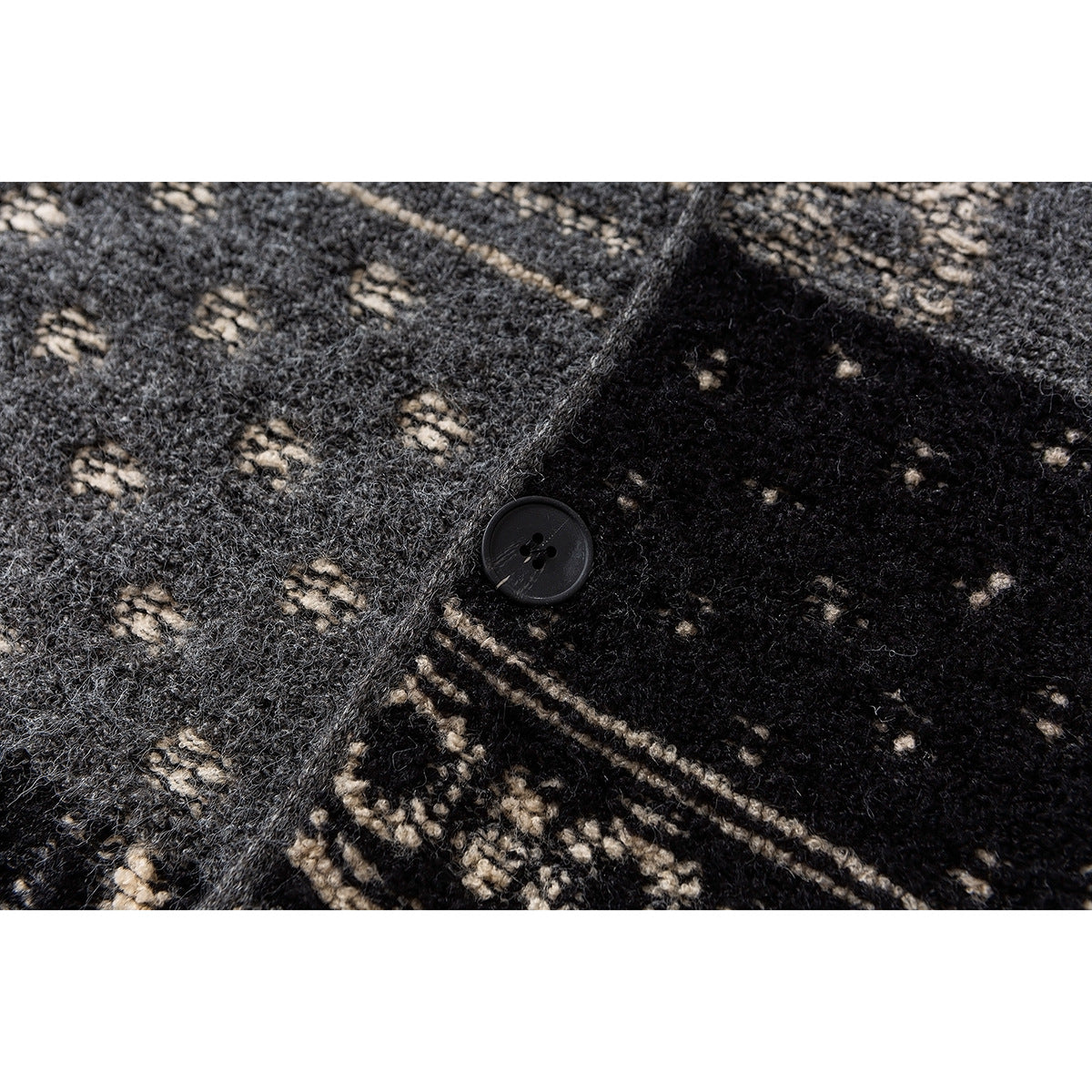 Close-up of a black button and textured black, gray, and cream patterned knit fabric.