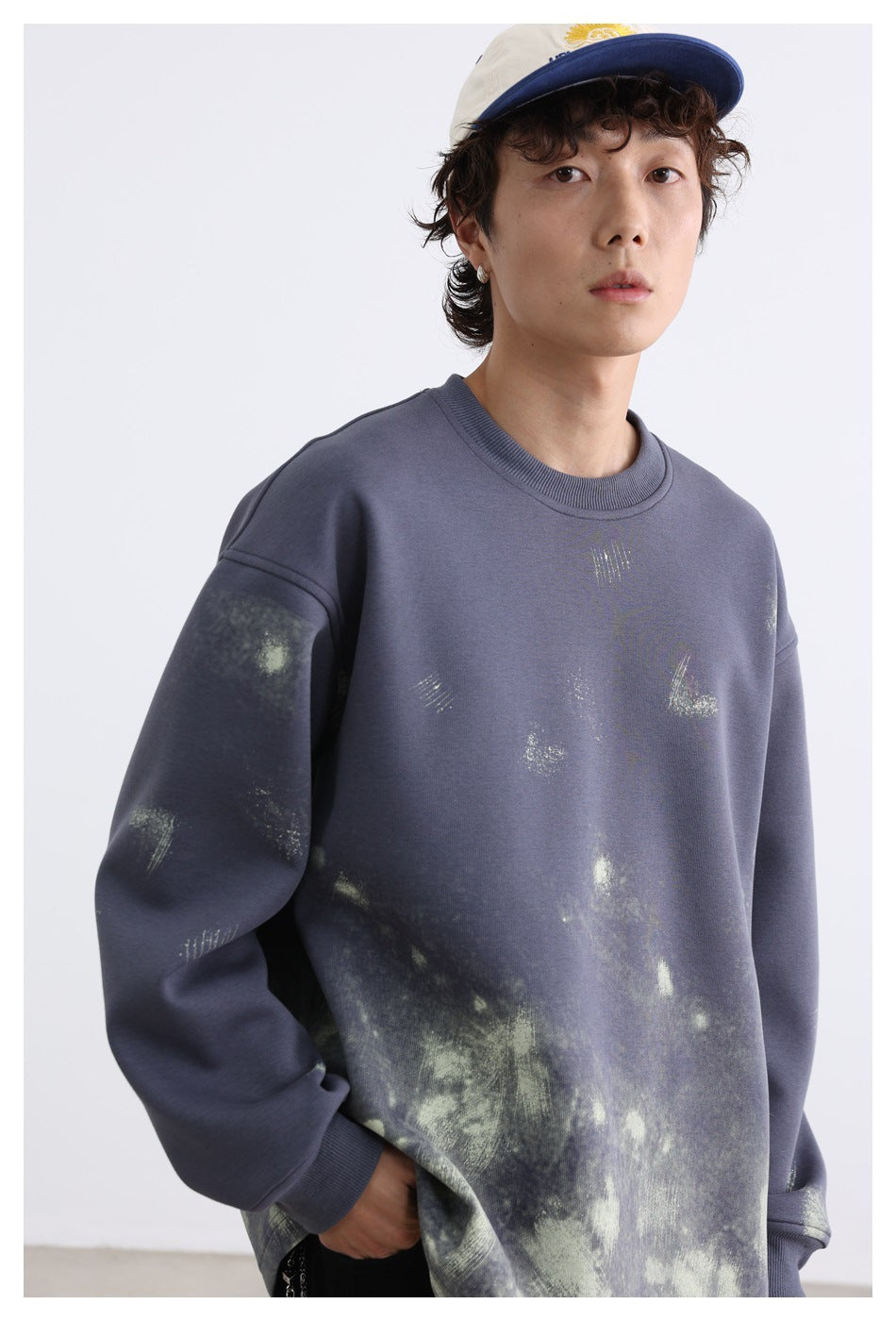 Close-up of model wearing a blue-gray crew-neck sweatshirt with pale green distressed print