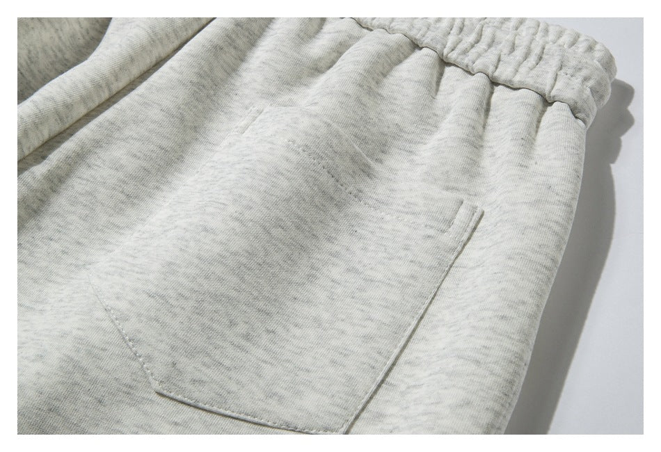 Close-up of light heather-gray sweatpants showing an elastic waistband and a stitched patch pocket.