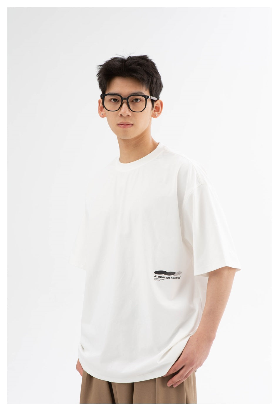 Model wearing an oversized white T-shirt with a small black chest graphic and tan trousers.