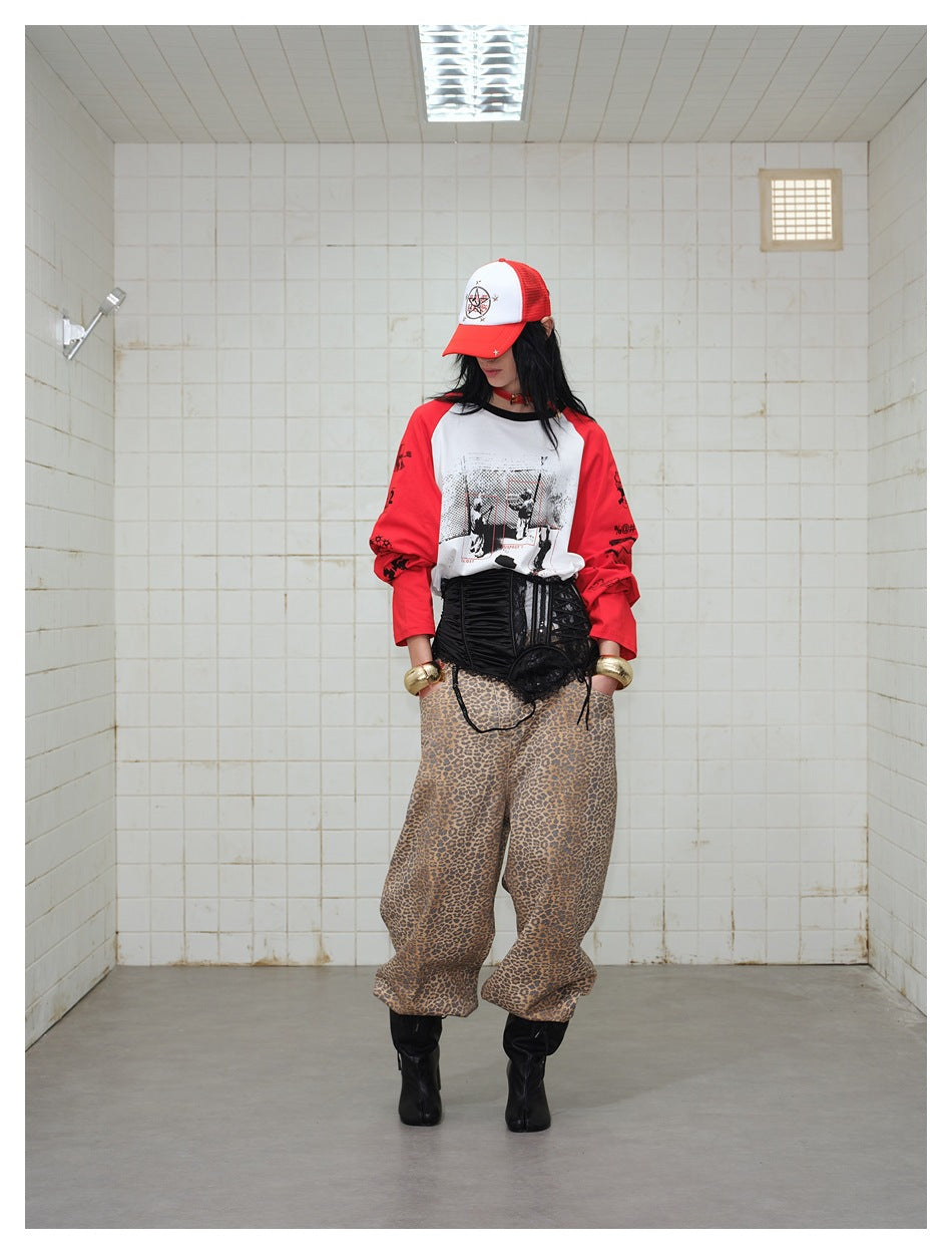 Model looking down in a white graphic raglan shirt with red sleeves and loose leopard-print trousers.