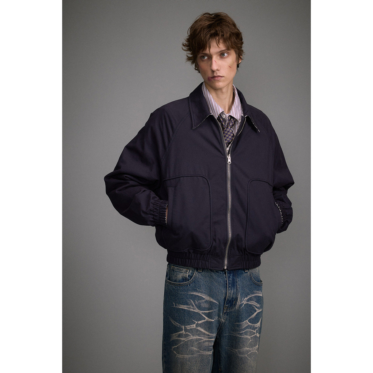 Model wearing a dark navy zip-front jacket with a pointed collar, large patch pockets and elastic cuffs.