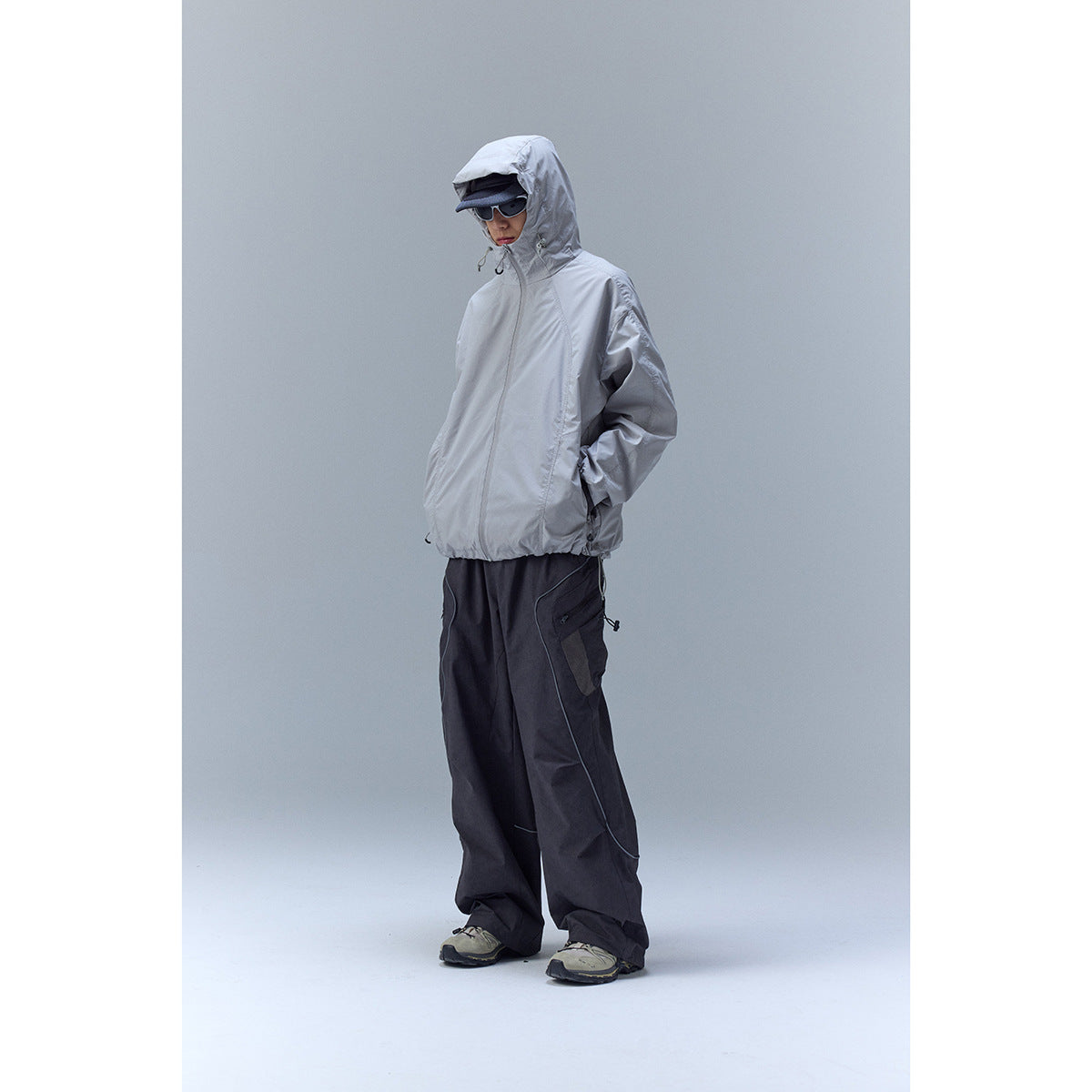 Model wearing a light gray hooded zip jacket and loose charcoal cargo trousers.