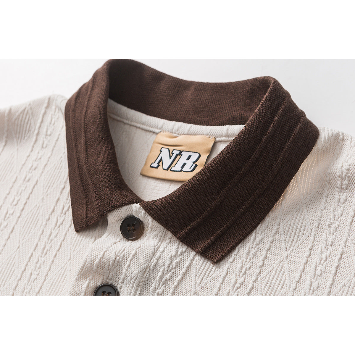 Close-up of a cream textured polo with a dark brown ribbed collar, dark buttons, and an NB neck label.