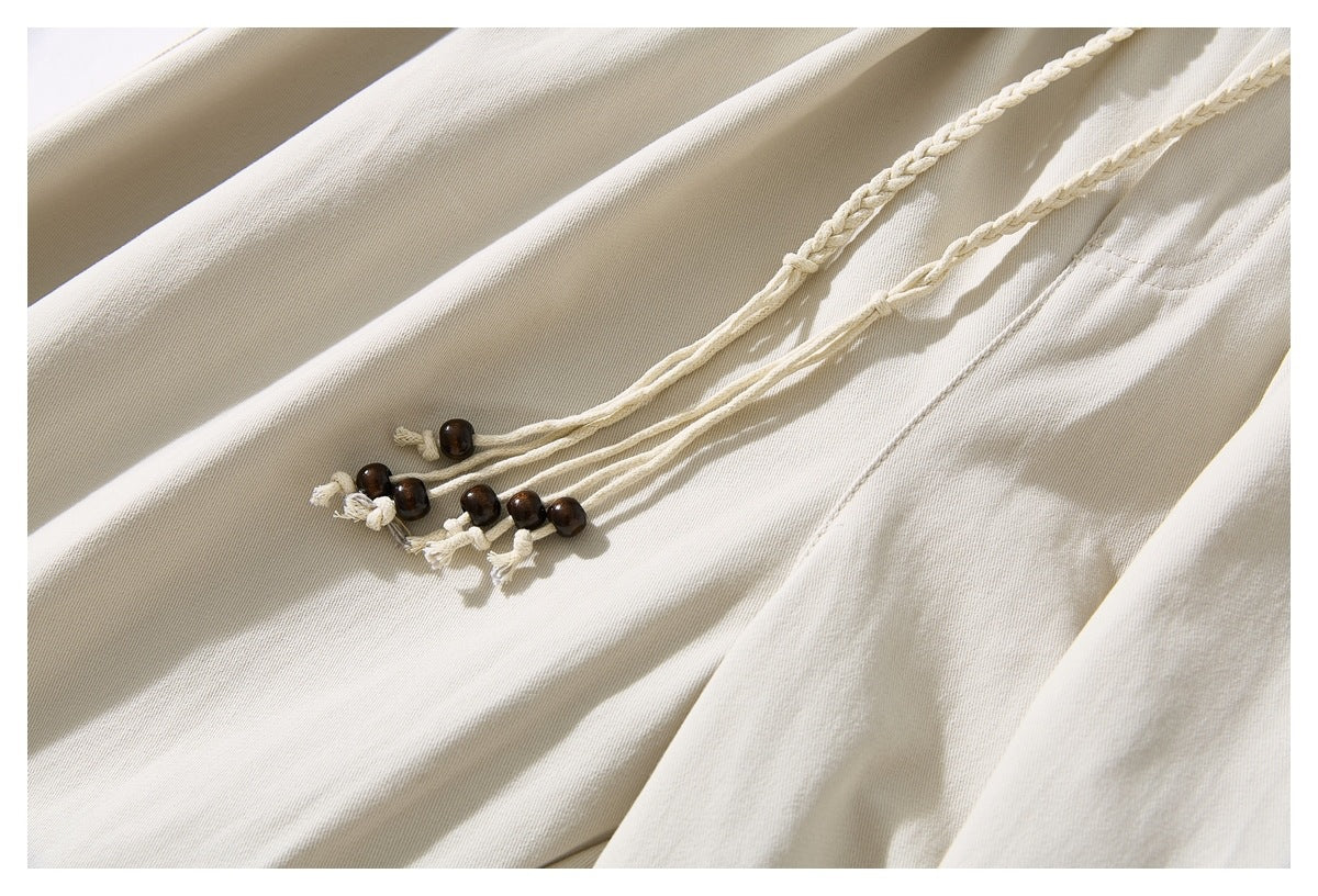 Close-up of cream trouser drawstrings with dark bead ends against the pleated fabric.