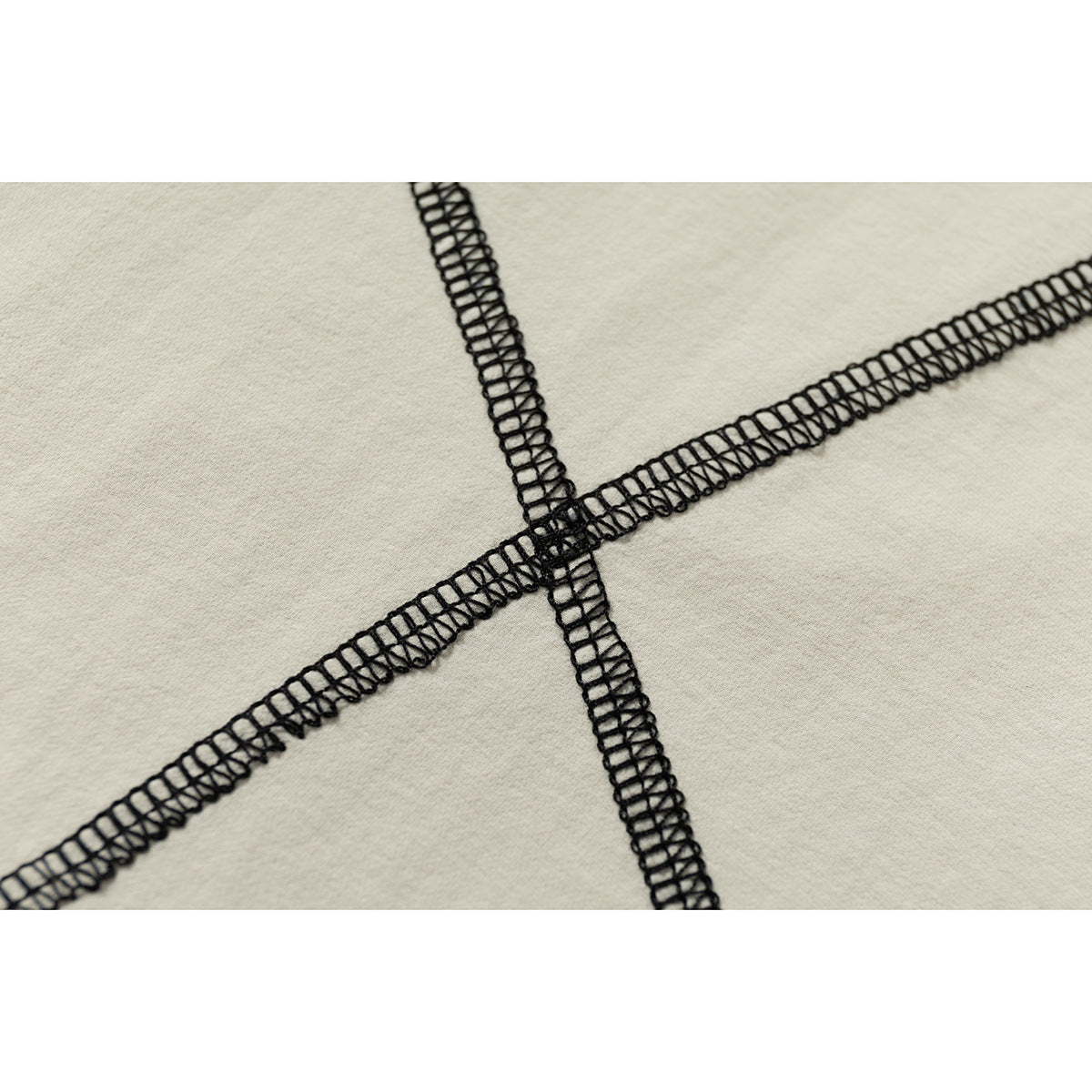 Close-up of intersecting black overlock seams on cream fabric.
