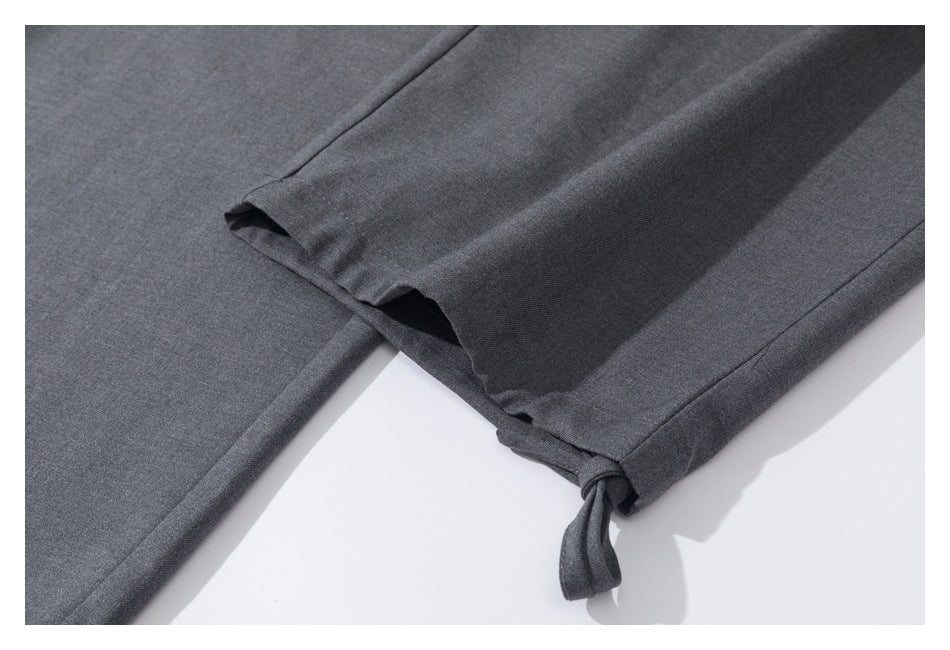 Close-up of charcoal gray trouser hems, showing a small side slit and a tied fabric tab.