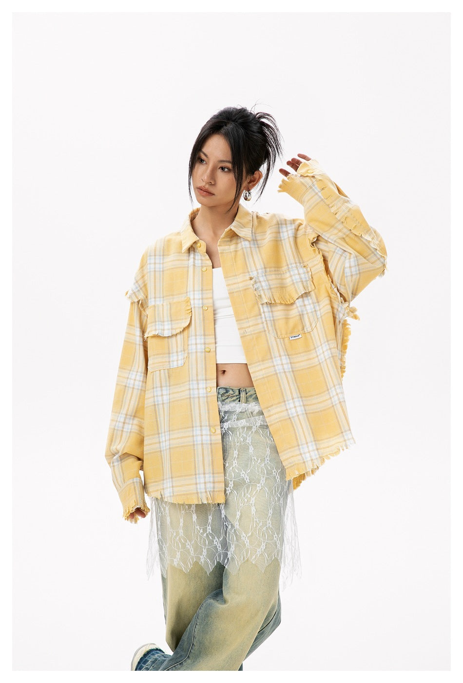 Model posing in an oversized yellow plaid button-up with frayed ruffle details and chest pockets, over a white top and