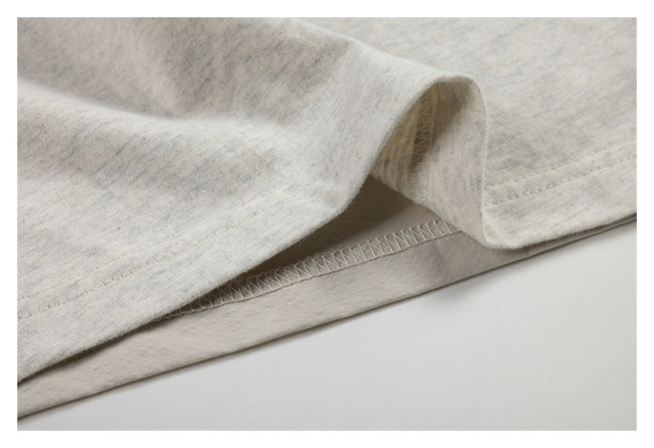 Close-up of a pale heather-gray garment's folded hem and visible overlock stitching.