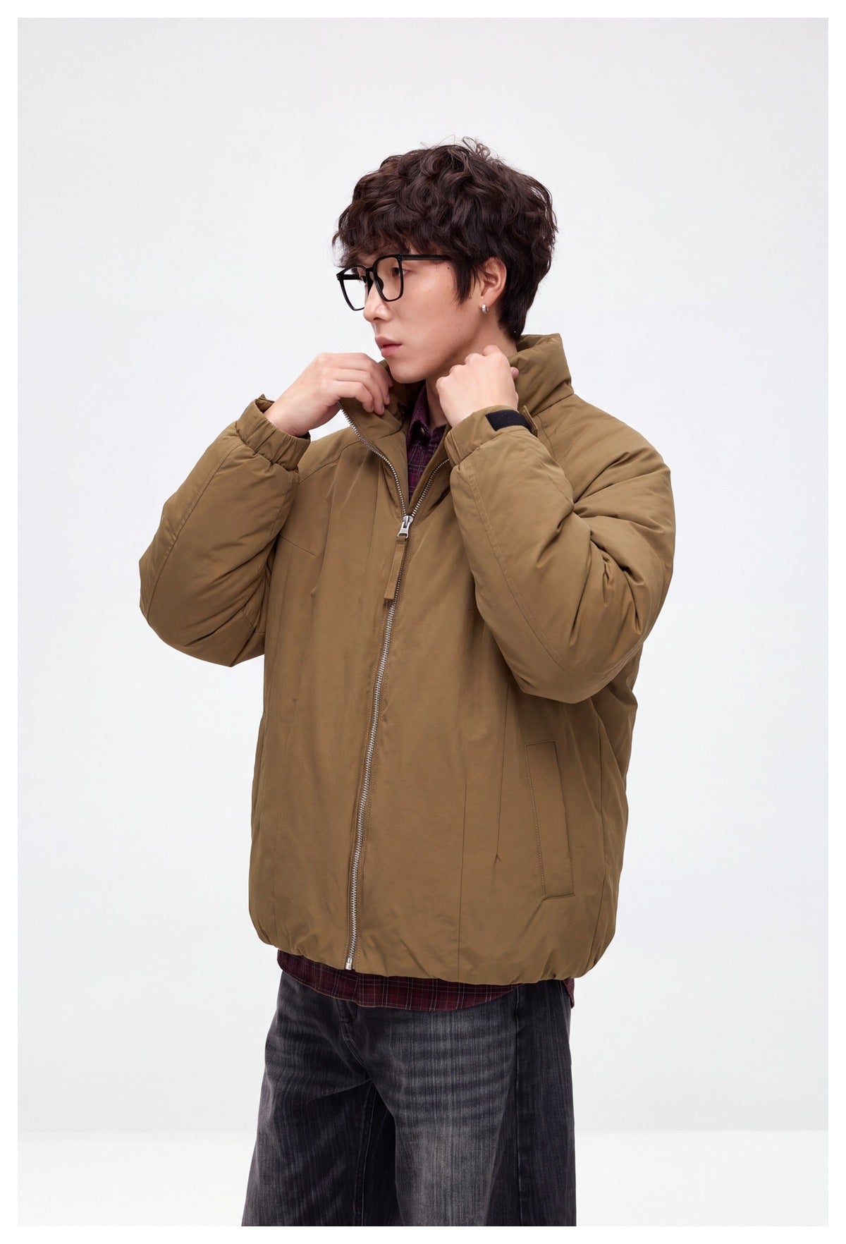 Man in tan brown padded stand-collar jacket over plaid shirt, side pose with hands at collar