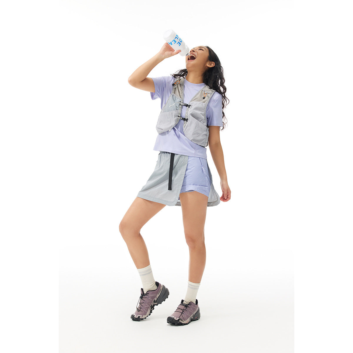 Model wearing a lavender T-shirt, gray utility vest and layered gray skirt over shorts.