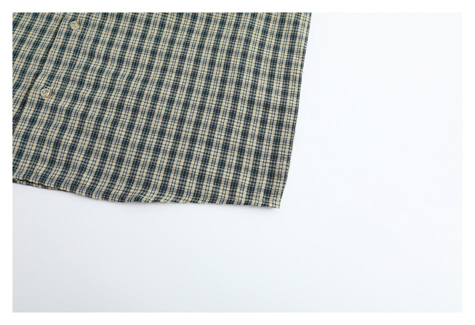 Cropped view of the plaid shirt's lower front hem and two buttons against a white background.