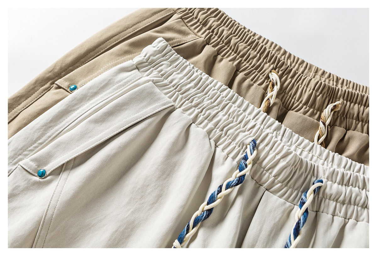 Close-up of khaki and light beige shorts showing elastic waistbands, braided drawstrings, and flap pockets with blue buttons.