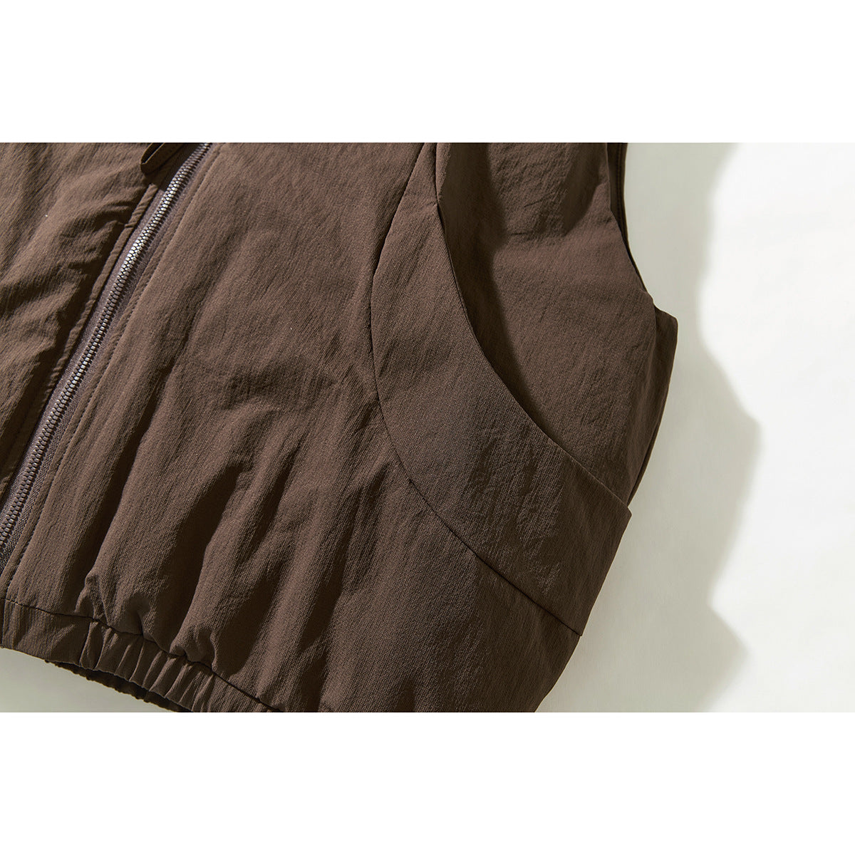 Close-up of the brown vest's curved side pocket, front zipper, and elastic hem.