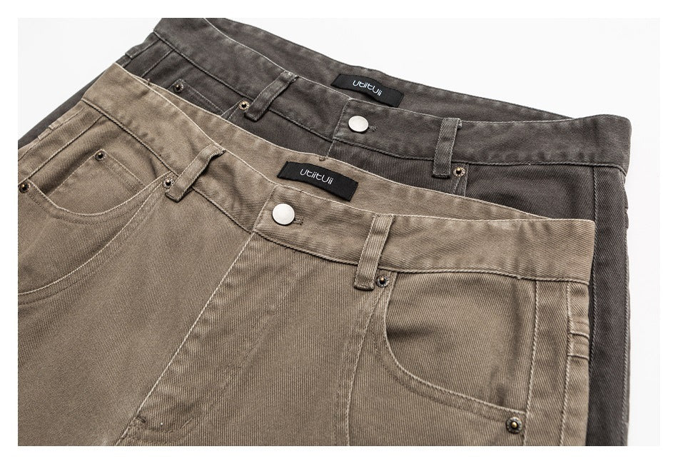 Close-up of two pairs of trousers in taupe and charcoal, showing front pockets, belt loops, buttons and waist labels.