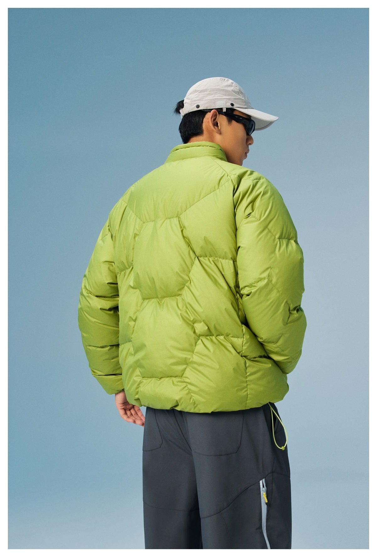 Back view of a model wearing a lime-green quilted jacket with a high collar and dark pants.