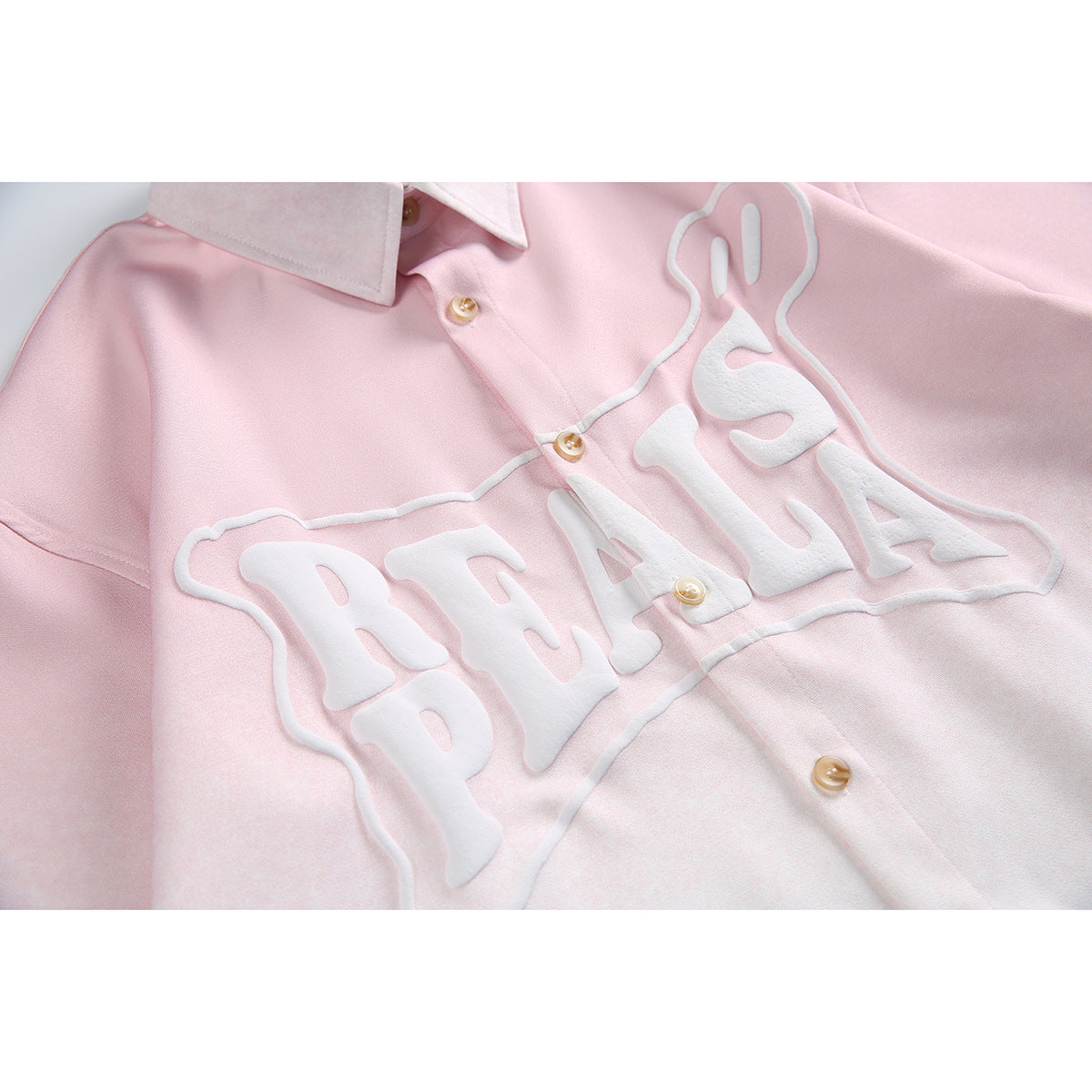 Close-up of the pink shirt’s raised white lettering, collar, and tan buttons.