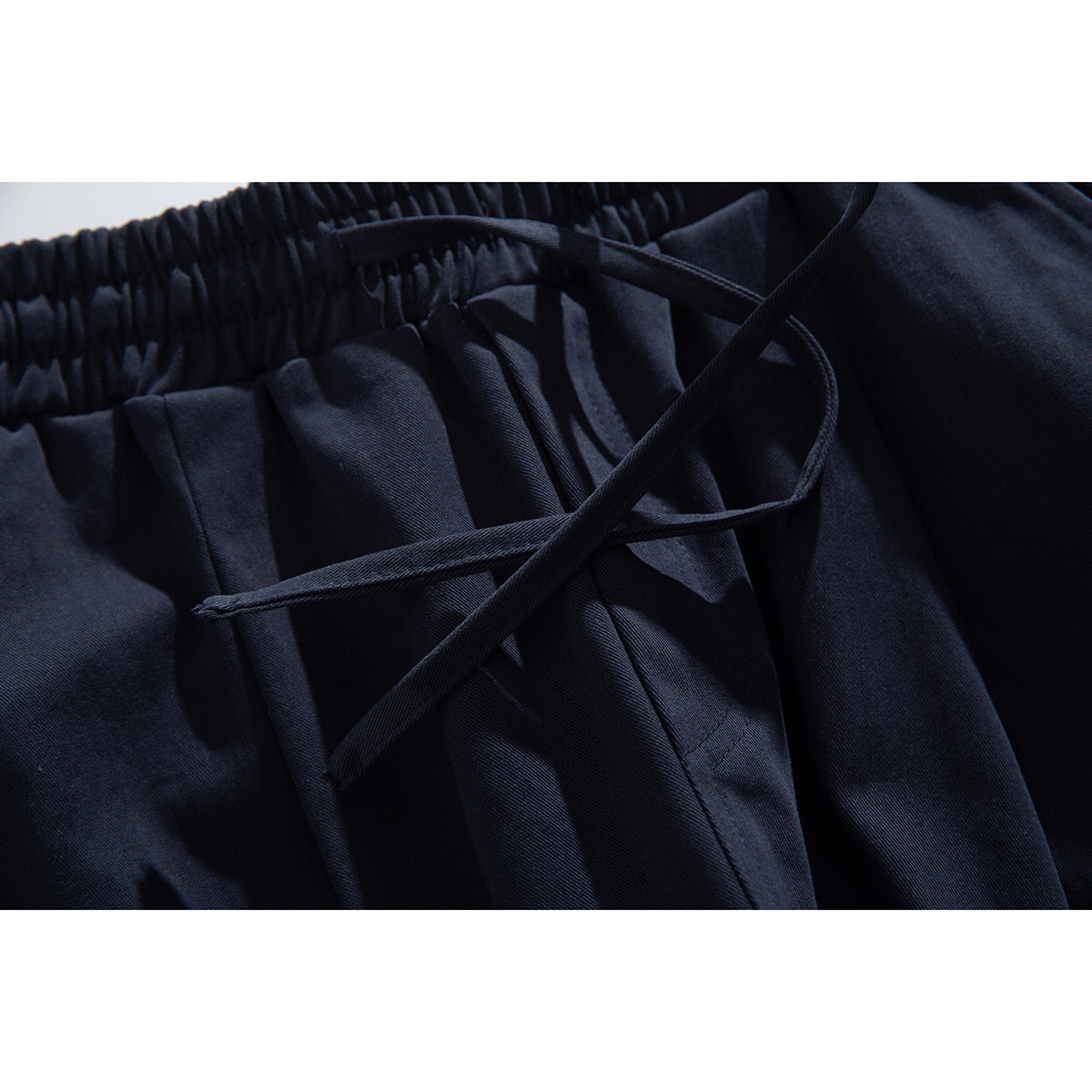 Close-up of dark navy pants with a gathered elastic waist and crossing drawstrings.