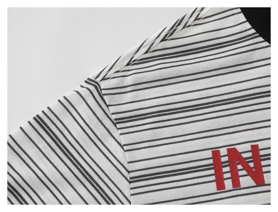 Close-up of a white shirt with thin black stripes, a shoulder seam, and red “IN” lettering.