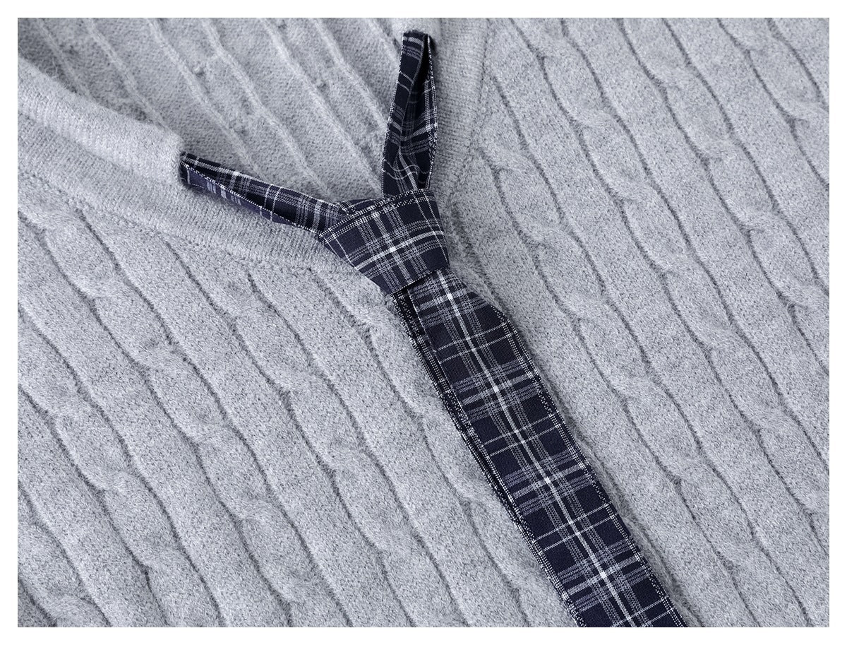 Close-up of a light gray cable-knit garment with a dark plaid ribbon detail.