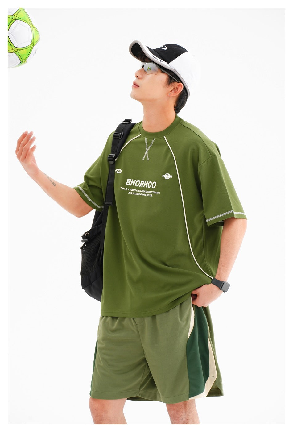 Man wearing an oversized olive-green sports T-shirt with white piping and matching color-block shorts.