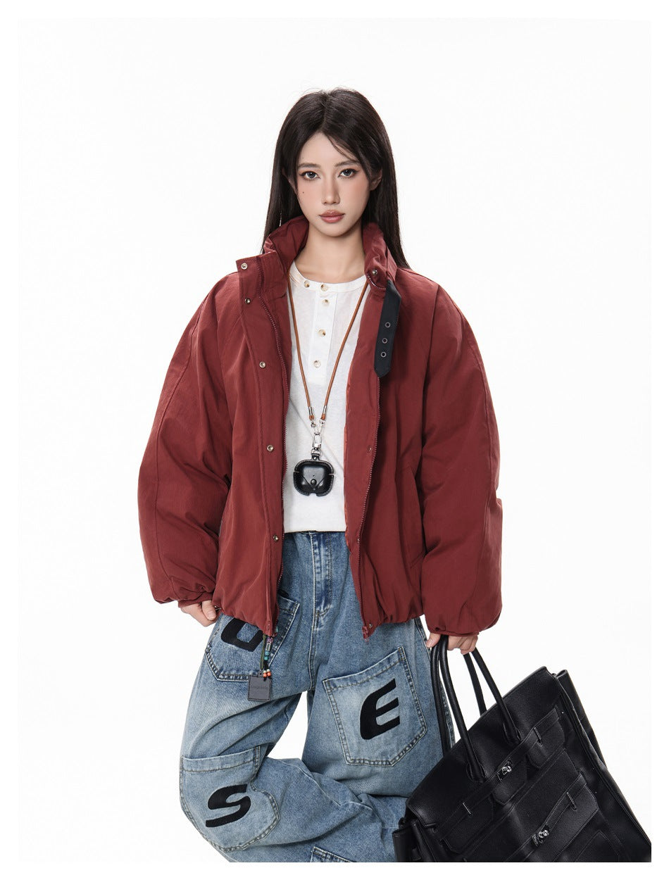 Model wearing an oversized burgundy jacket over a white top and loose blue graphic jeans.