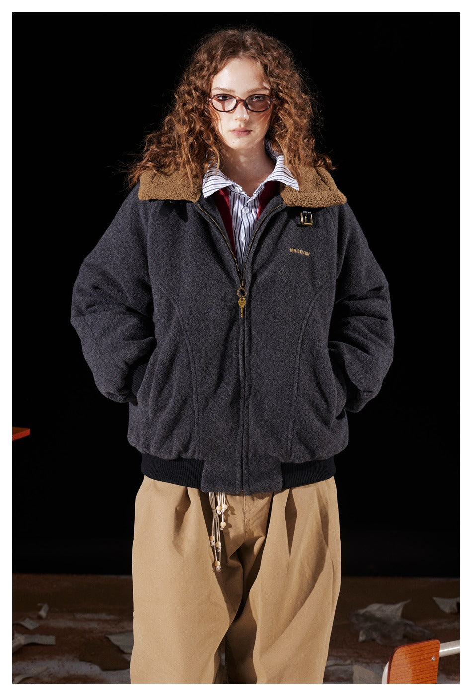 Front view of a model wearing a charcoal zip-up jacket with a tan fleece collar and black ribbed trim.