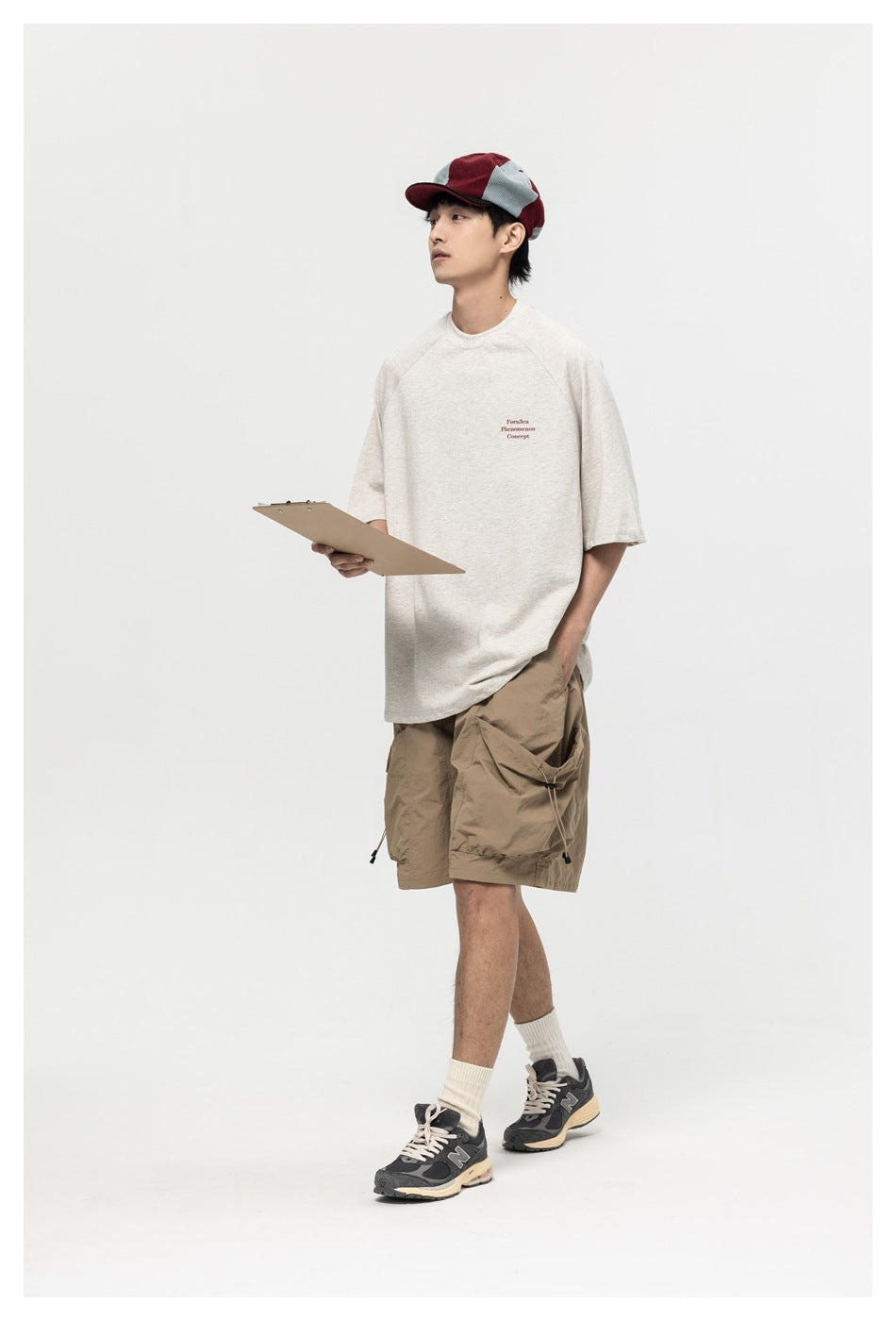 Model wearing light gray raglan-sleeve T-shirt with small chest text print, holding a clipboard