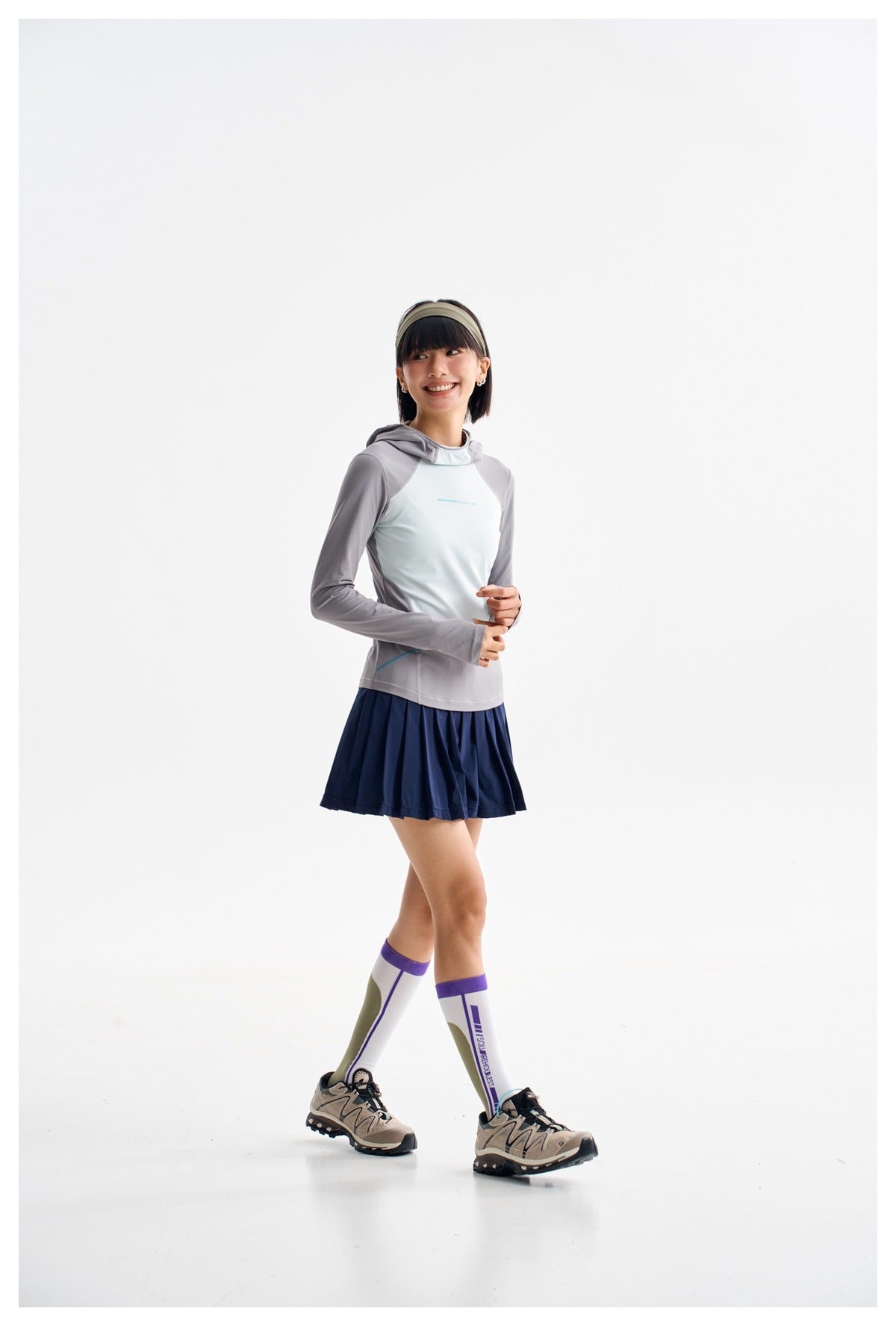Model in a pale mint and gray hooded top with a navy pleated skirt, knee-high socks, and sneakers.