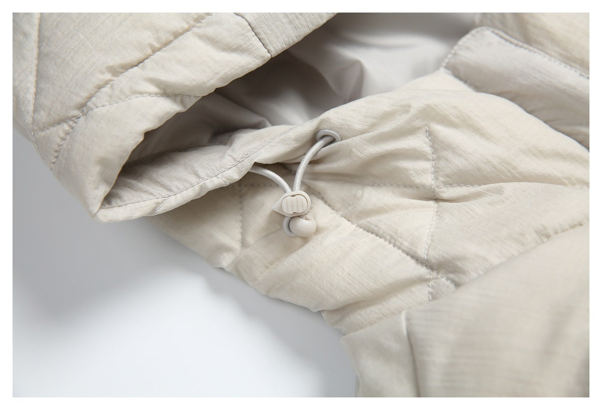 Close-up of the ivory coat's hood drawcord and toggle against quilted fabric.