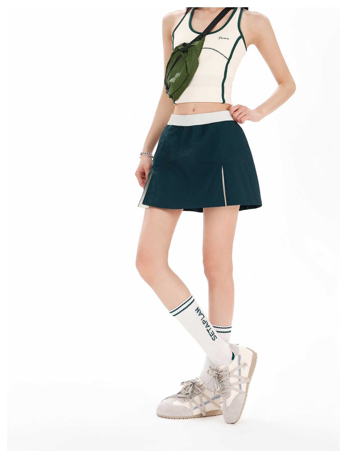 Model wearing a dark teal athletic skirt with a white waistband and narrow light-colored side insets, shown at a