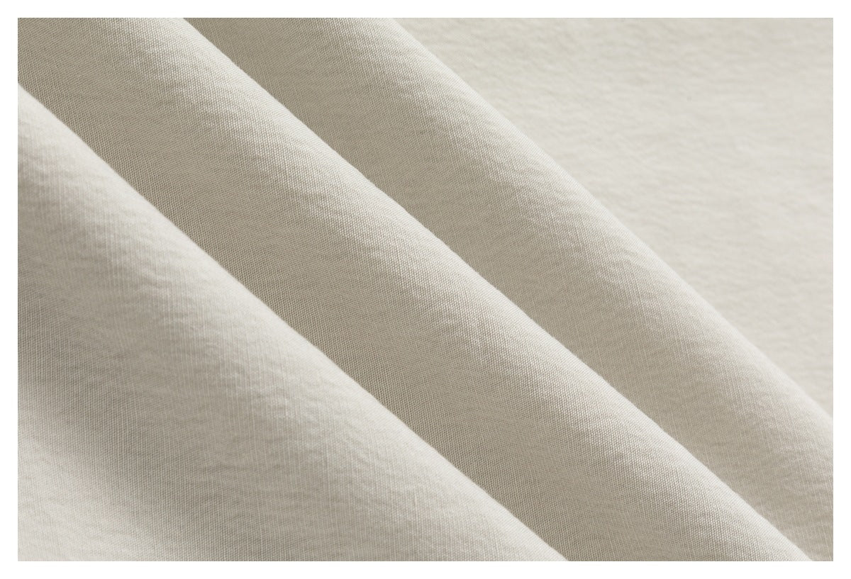 Close-up of softly draped light beige fabric showing its fine woven texture.