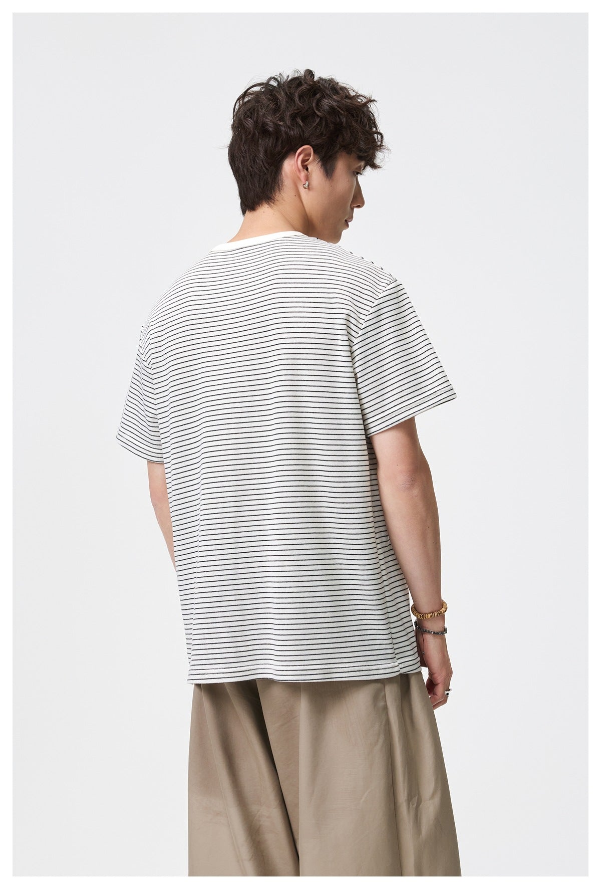 Back view of a model wearing an ivory short-sleeve T-shirt with thin black stripes and beige trousers.