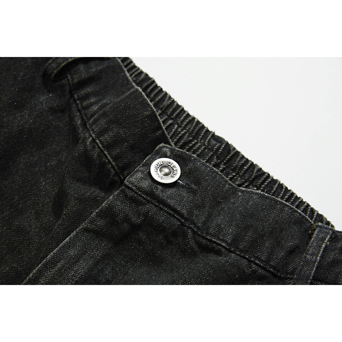 Close-up of black denim shorts showing the gathered waistband, belt loop, stitching and silver button.