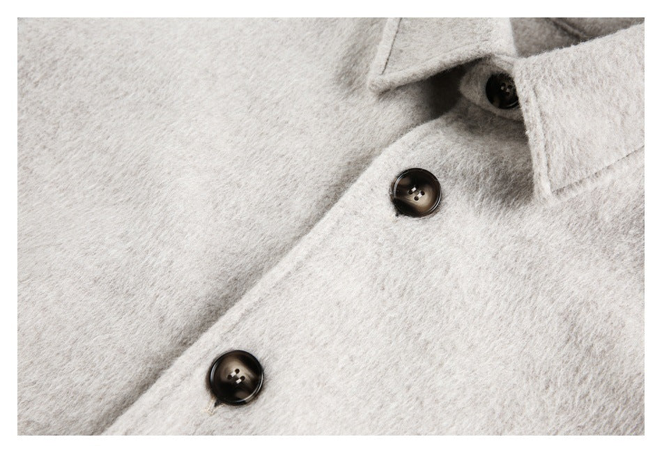 Close-up of a cream coat's front placket with dark buttons and overlapping fabric.