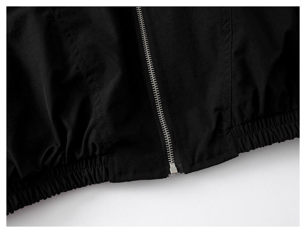 Close-up of the black jacket's silver front zipper and gathered elastic hem.