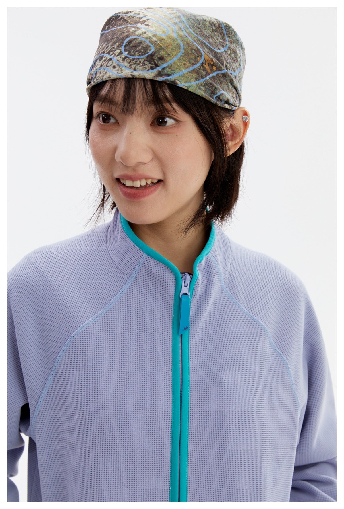 Close-up of the lavender jacket’s textured surface, teal-trimmed collar and zipper, with a patterned headscarf visible.