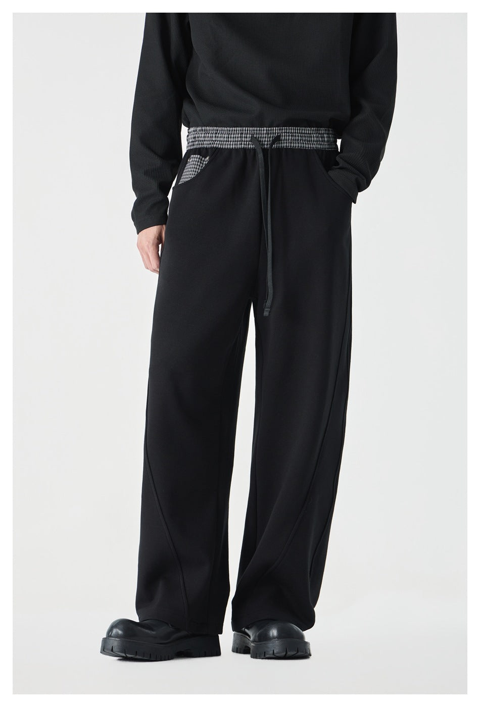 Front view of a model wearing black wide-leg pants with a checked waistband, drawstring, and checked pocket.