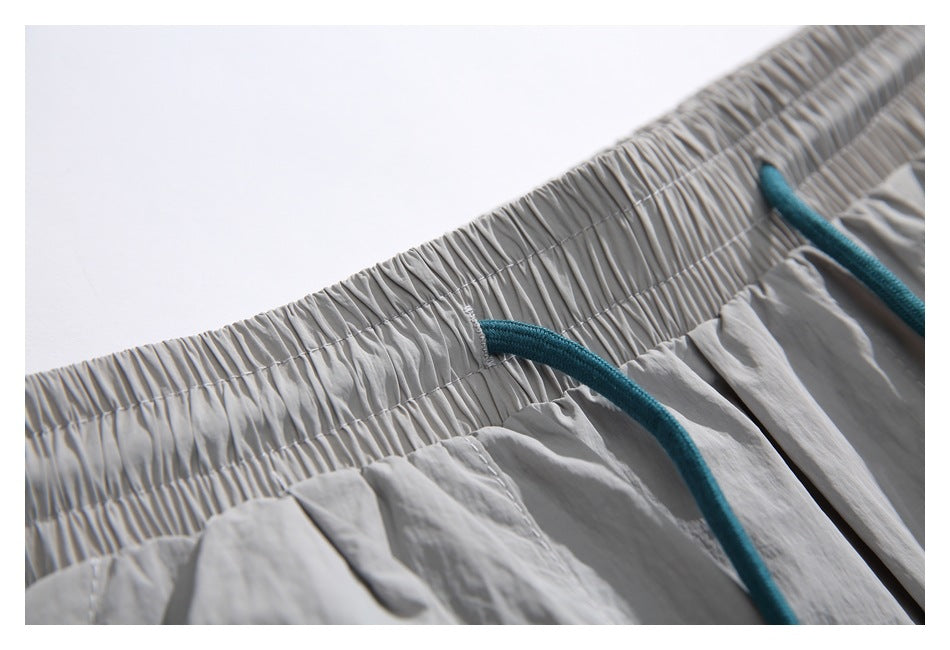 Close-up of the gathered waistband and teal drawstring attachment on light gray shorts.