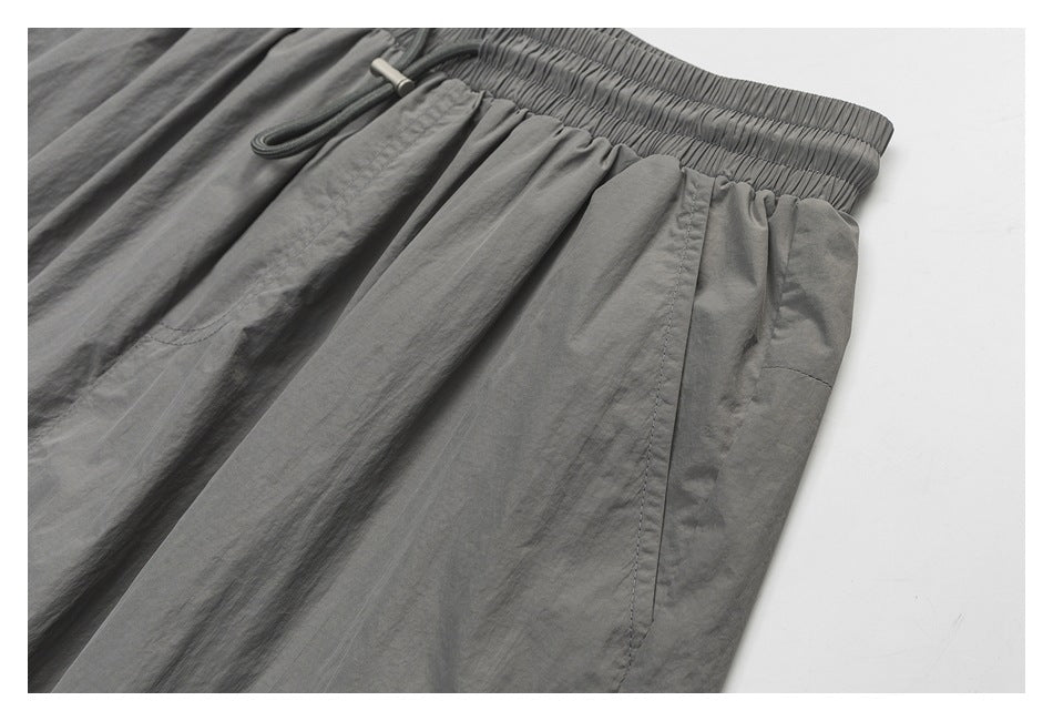 Close-up of gray shorts showing the elastic waistband, drawcord, and side pocket seam.