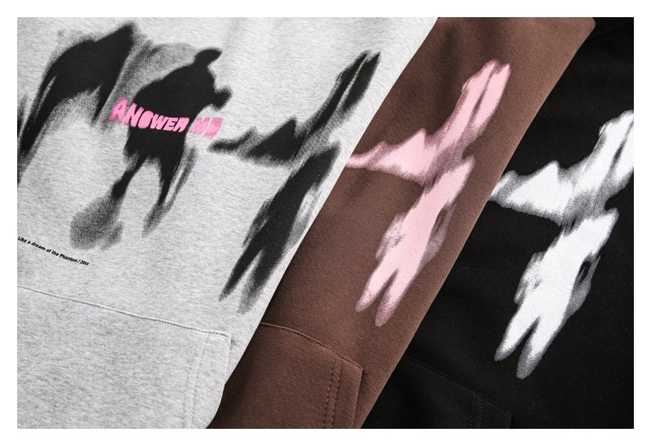 Close-up of three hoodies in gray, brown, and black, each with abstract brushstroke graphics and a kangaroo pocket.