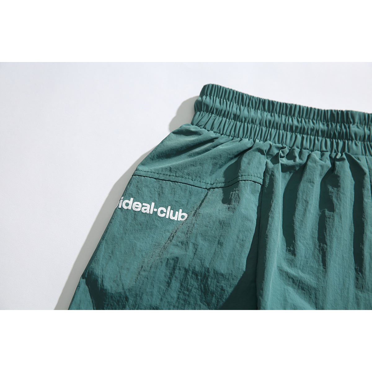 Close-up of the teal shorts' gathered waistband and white ideal-club logo.