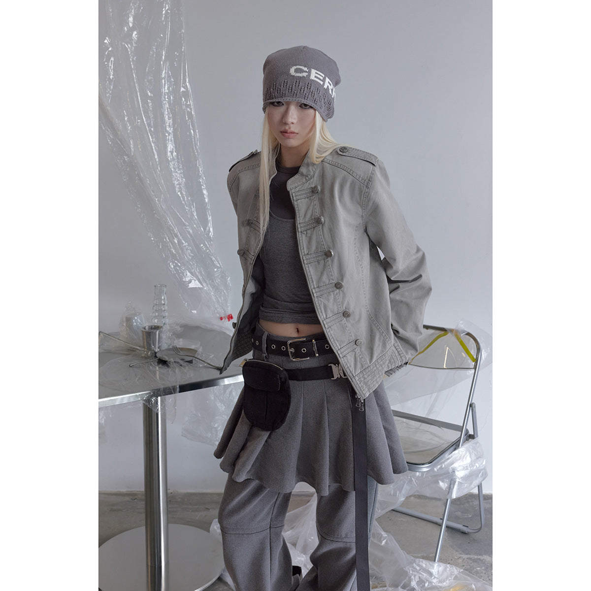 Model wearing a light gray military-style jacket with horizontal button tabs and a front zipper.