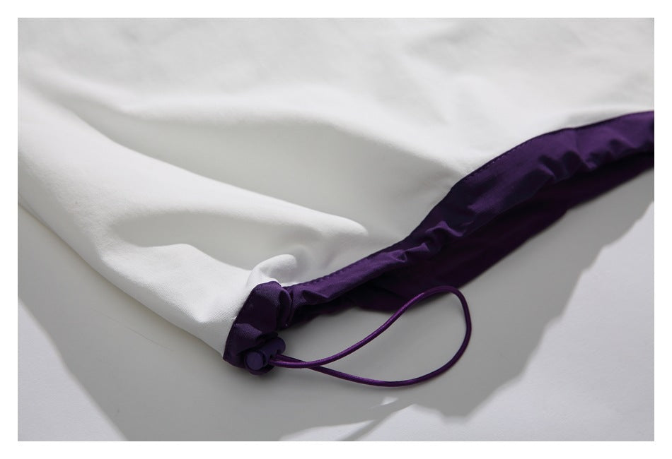 Close-up of white garment fabric with a deep purple bound edge and adjustable drawcord toggle.